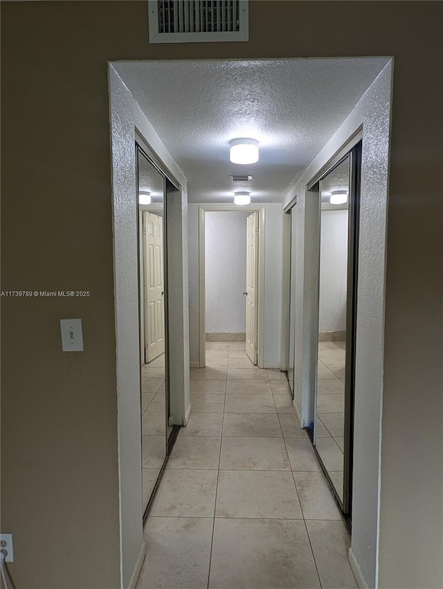 hall with a textured ceiling and light tile patterned floors