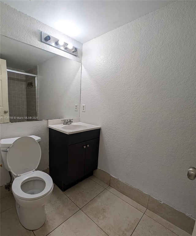 bathroom with tile patterned flooring, vanity, tiled shower, and toilet