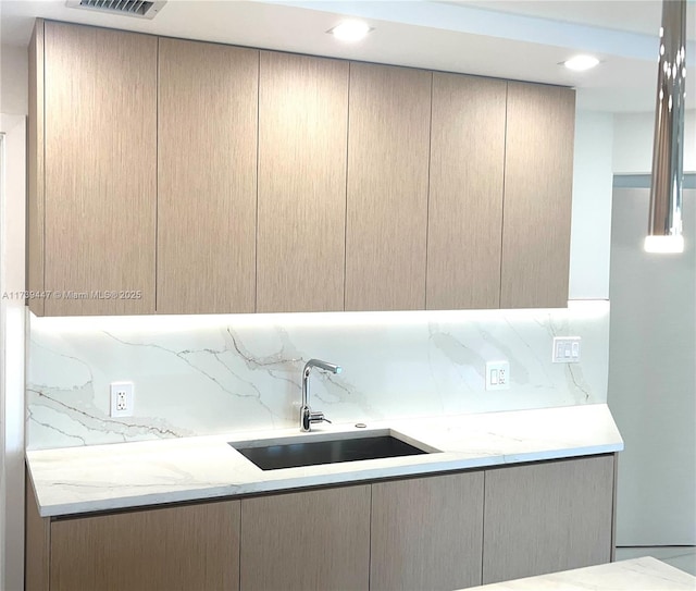 kitchen with a sink, visible vents, light stone countertops, tasteful backsplash, and modern cabinets