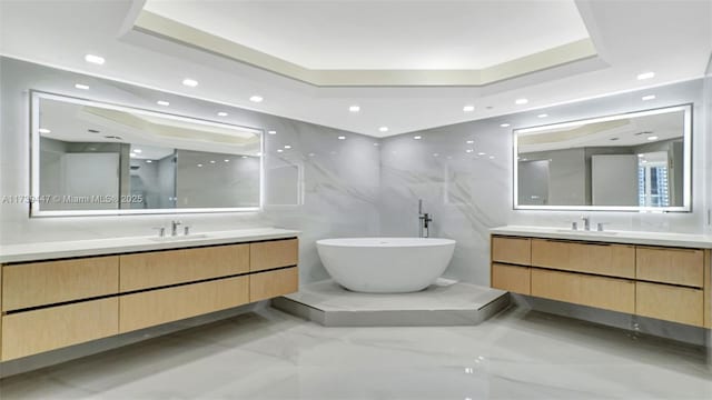 full bathroom with a tray ceiling, marble finish floor, a sink, and a freestanding bath