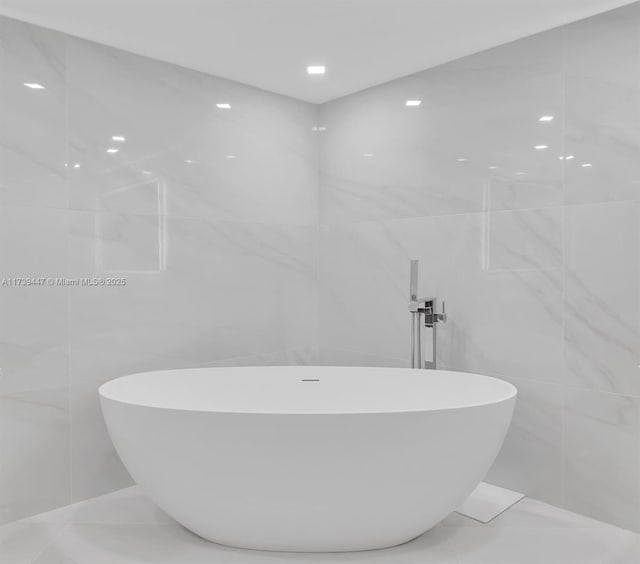 full bath featuring a freestanding tub, tile walls, and marble finish floor