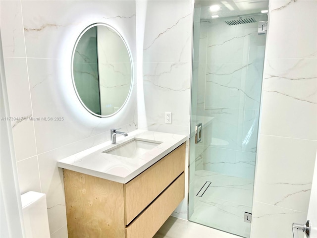 bathroom featuring a marble finish shower, tile walls, and vanity