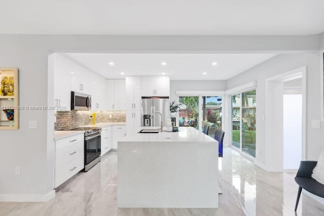 kitchen with sink, white cabinetry, appliances with stainless steel finishes, a kitchen island with sink, and backsplash