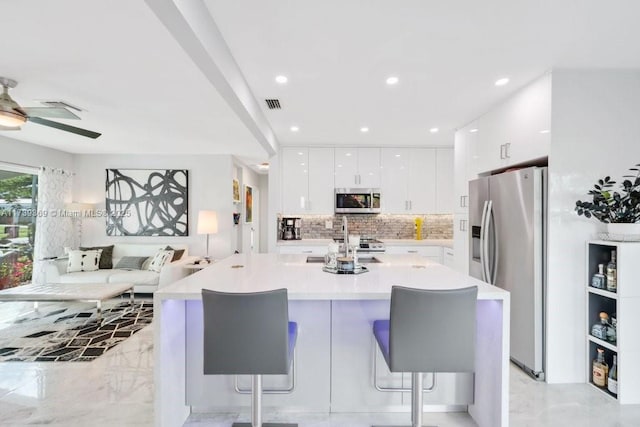 kitchen with a breakfast bar area, white cabinetry, stainless steel appliances, a kitchen island with sink, and backsplash