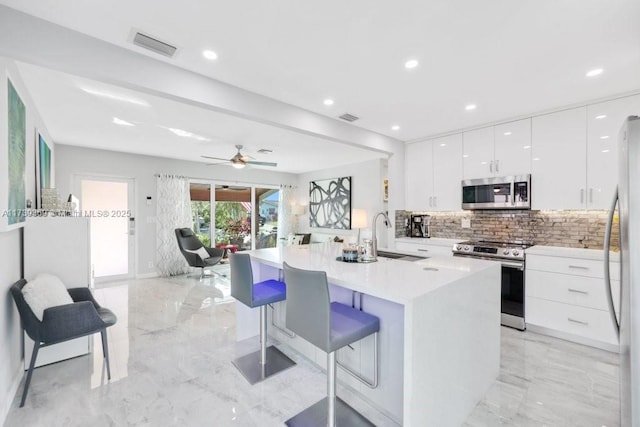 kitchen featuring sink, a breakfast bar, appliances with stainless steel finishes, white cabinets, and a center island with sink