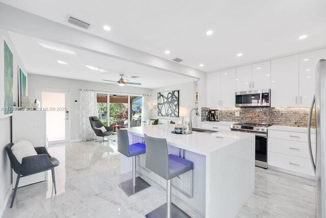 kitchen featuring appliances with stainless steel finishes, beamed ceiling, white cabinetry, sink, and a kitchen island with sink