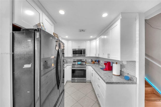 kitchen with appliances with stainless steel finishes, white cabinets, backsplash, light tile patterned floors, and light stone counters