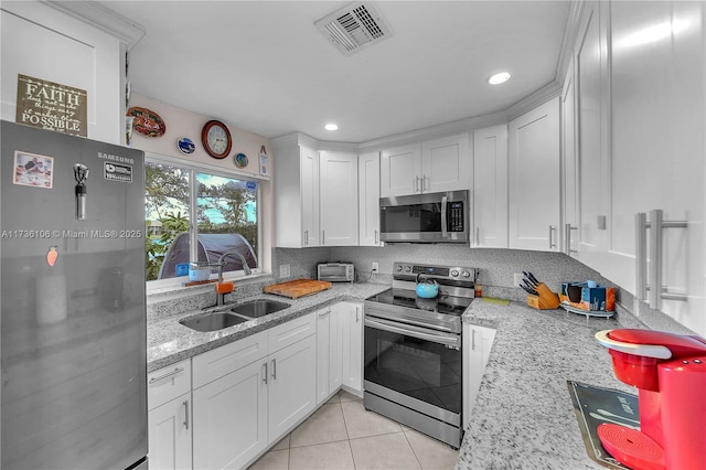 kitchen featuring sink, appliances with stainless steel finishes, white cabinetry, light stone countertops, and light tile patterned flooring