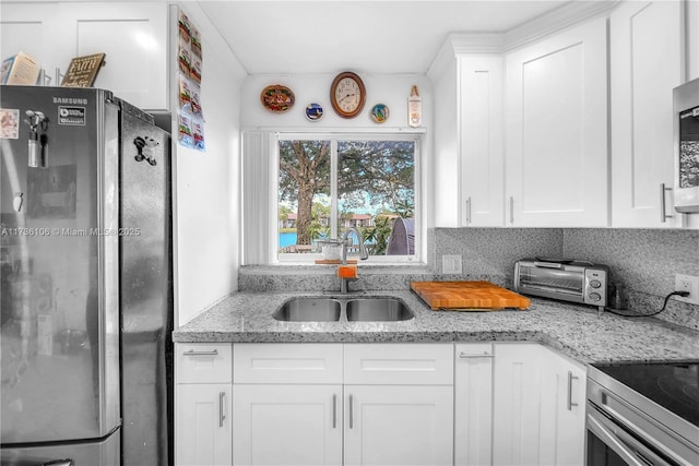 kitchen featuring sink, light stone counters, white cabinets, and stainless steel refrigerator