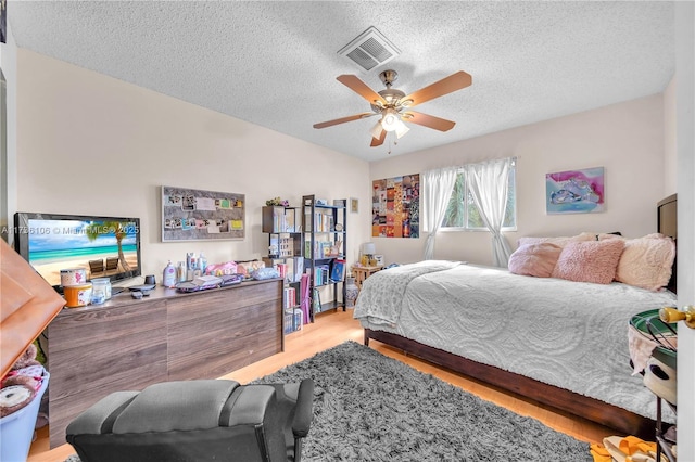 bedroom featuring ceiling fan, vaulted ceiling, a textured ceiling, and light wood-type flooring