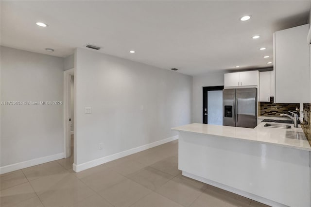 kitchen featuring stainless steel refrigerator with ice dispenser, sink, white cabinetry, kitchen peninsula, and decorative backsplash