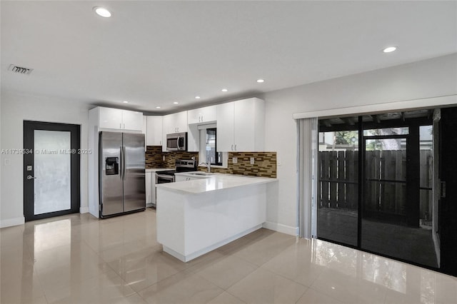 kitchen with sink, appliances with stainless steel finishes, white cabinets, decorative backsplash, and kitchen peninsula