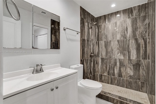 bathroom with tiled shower, vanity, and toilet