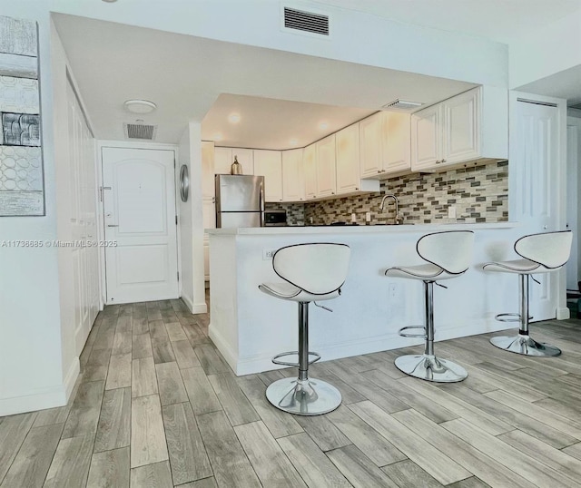 kitchen featuring tasteful backsplash, white cabinetry, stainless steel fridge, and a kitchen breakfast bar