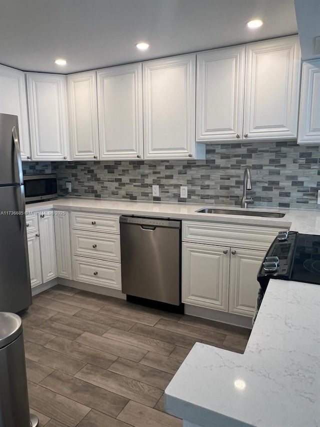 kitchen with appliances with stainless steel finishes, white cabinetry, sink, backsplash, and dark wood-type flooring