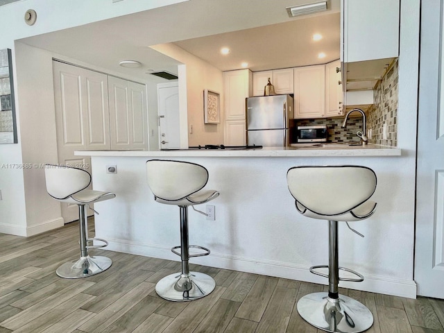 kitchen with white cabinetry, appliances with stainless steel finishes, kitchen peninsula, and light hardwood / wood-style flooring