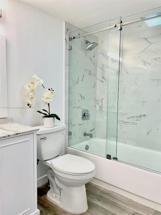 full bathroom with hardwood / wood-style flooring, bath / shower combo with glass door, vanity, and toilet