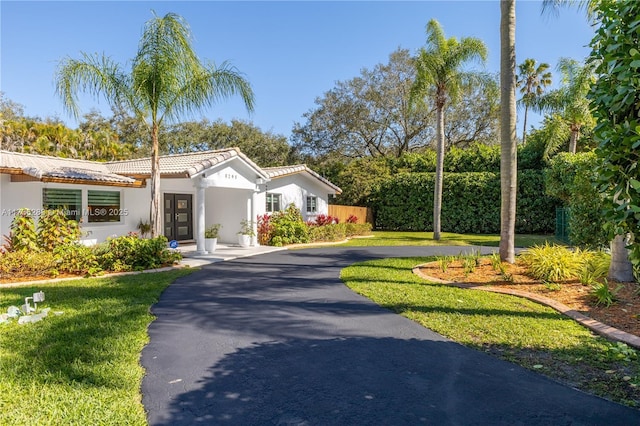 view of front of house featuring a tile roof, aphalt driveway, french doors, a front lawn, and stucco siding