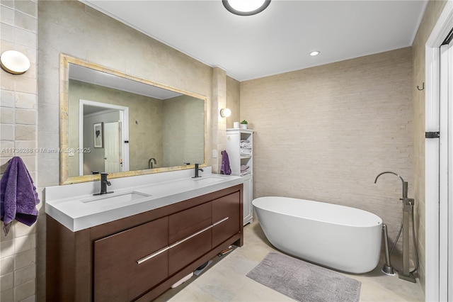 bathroom featuring a sink, tile walls, a freestanding bath, and double vanity