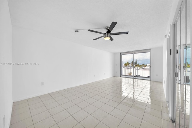 spare room featuring ceiling fan, a wall of windows, a textured ceiling, and light tile patterned floors