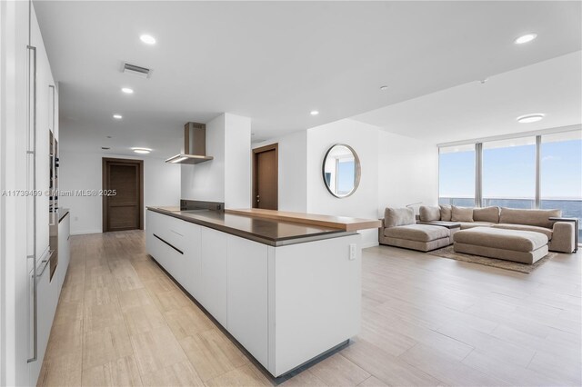 kitchen featuring wall chimney range hood, light hardwood / wood-style flooring, a wall of windows, white cabinetry, and a water view