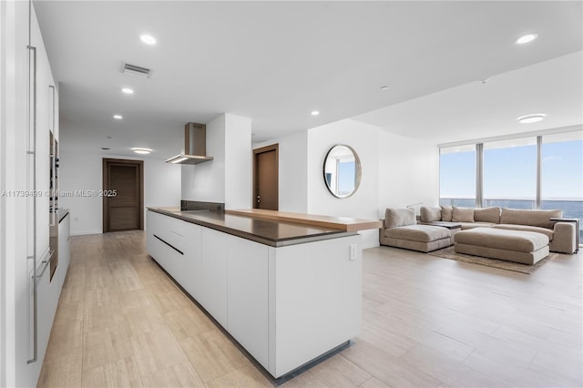 kitchen featuring dark countertops, visible vents, white cabinets, wall chimney range hood, and modern cabinets