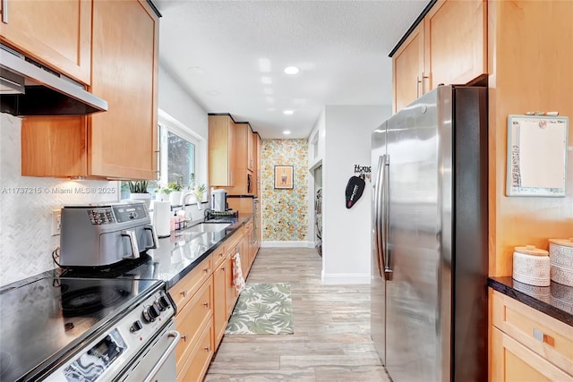 kitchen featuring sink, dark stone counters, stainless steel appliances, a textured ceiling, and light hardwood / wood-style flooring