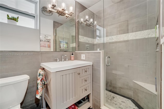 bathroom with a shower with shower door, tile walls, vanity, toilet, and an inviting chandelier