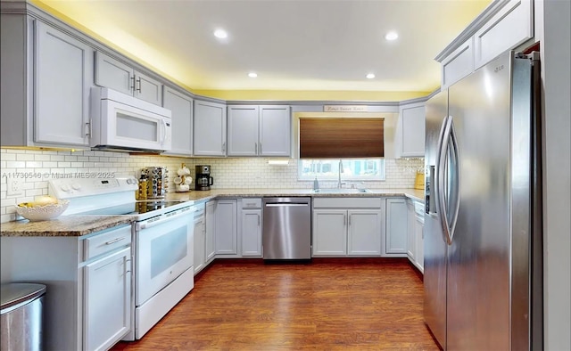 kitchen with dark wood-type flooring, sink, light stone counters, appliances with stainless steel finishes, and decorative backsplash