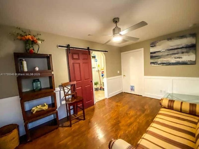 living room with ceiling fan, a barn door, and dark hardwood / wood-style flooring