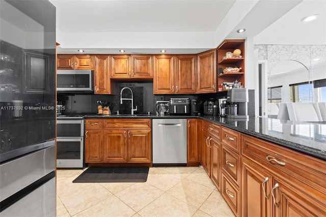 kitchen with dark stone counters, appliances with stainless steel finishes, a sink, and brown cabinets