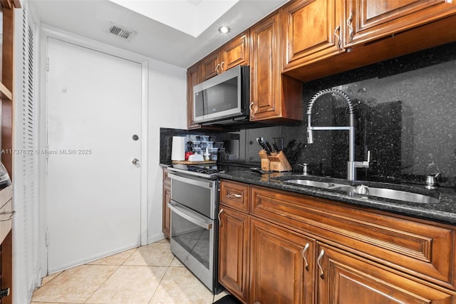 kitchen featuring stainless steel appliances, dark stone countertops, a sink, and brown cabinets