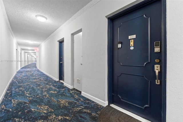 hallway featuring baseboards, dark carpet, a textured ceiling, and a textured wall