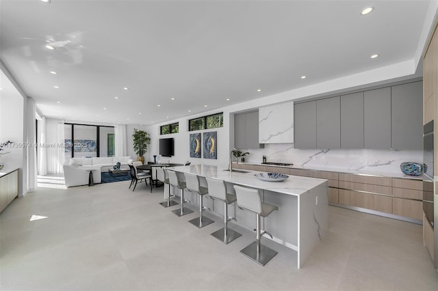 kitchen with gray cabinetry, a kitchen breakfast bar, a large island, light stone countertops, and backsplash