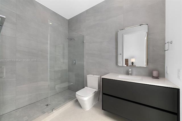 bathroom with a tile shower, tile walls, vanity, and toilet