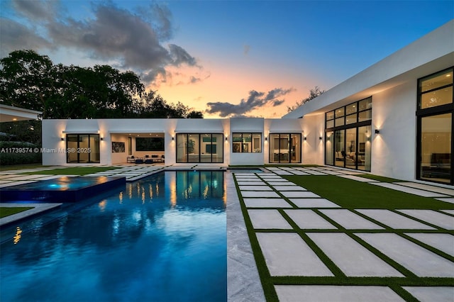 pool at dusk with a patio and an in ground hot tub