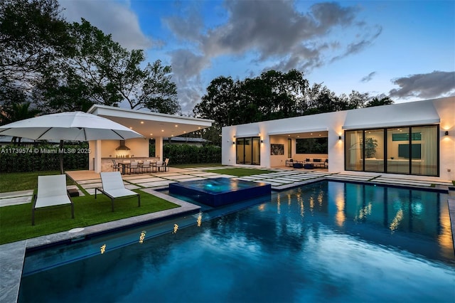 pool at dusk featuring an in ground hot tub, an outdoor bar, and a patio area