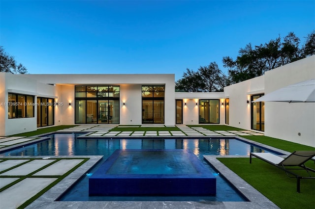 pool at dusk featuring a patio, an in ground hot tub, and a lawn