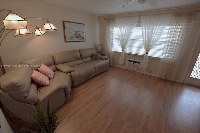 living room featuring wood-type flooring, a wall mounted air conditioner, ceiling fan, and a textured ceiling