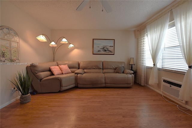 living room with ceiling fan, wood-type flooring, a wall mounted AC, and a textured ceiling