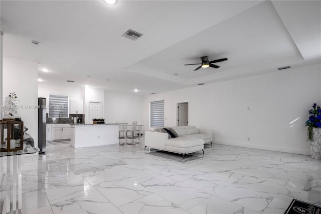 living room featuring sink, ceiling fan, and a tray ceiling