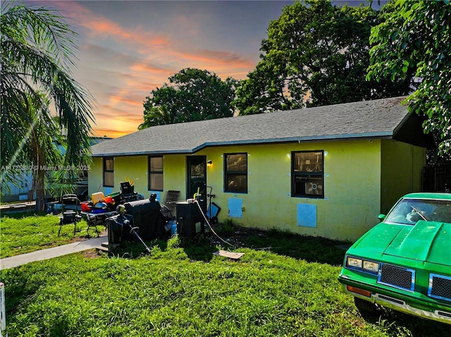 ranch-style house featuring roof with shingles, a lawn, and stucco siding