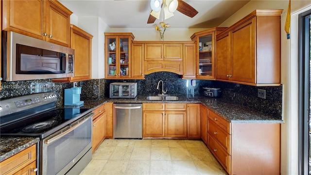 kitchen featuring dark stone counters, appliances with stainless steel finishes, backsplash, and a sink