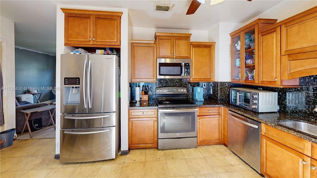 kitchen with visible vents, decorative backsplash, appliances with stainless steel finishes, brown cabinets, and dark stone countertops