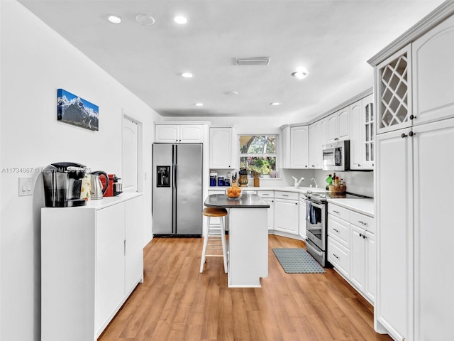 kitchen with a center island, appliances with stainless steel finishes, white cabinetry, light wood-type flooring, and a kitchen bar