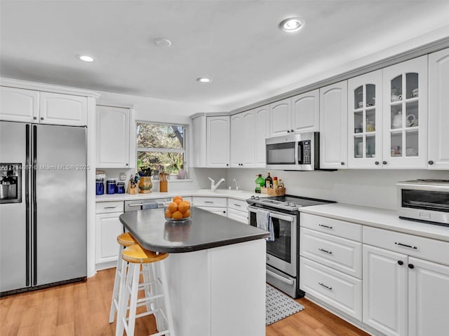 kitchen with a breakfast bar area, a toaster, light wood-style floors, appliances with stainless steel finishes, and glass insert cabinets