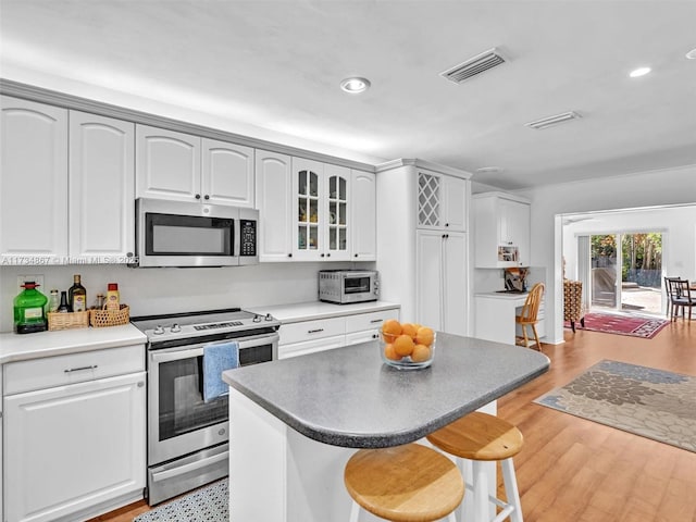 kitchen with stainless steel appliances, visible vents, a kitchen island, light wood-type flooring, and a kitchen bar