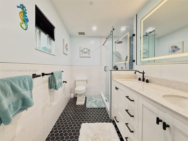 bathroom featuring tile walls, vanity, toilet, a shower with door, and tile patterned floors