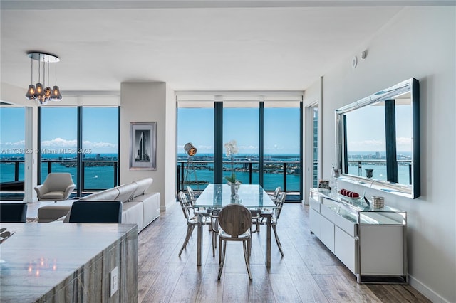 dining area with a water view, an inviting chandelier, a wall of windows, and light hardwood / wood-style flooring