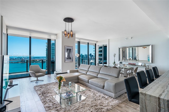 living room featuring light hardwood / wood-style flooring, a wall of windows, a chandelier, and a water view